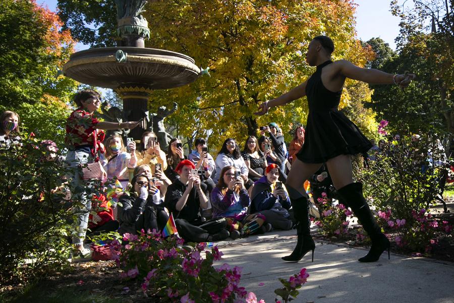 A person dances in front of a crowd by a fountain with fall trees in the background.